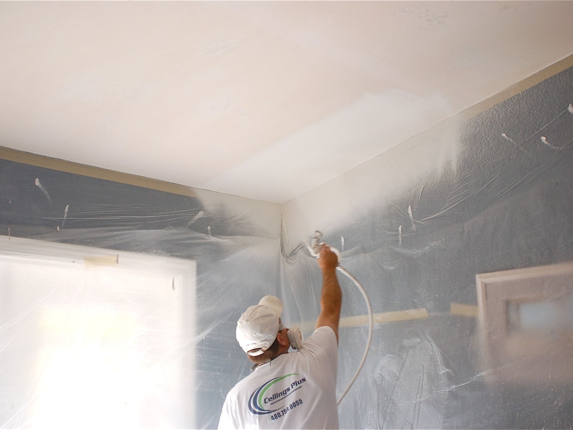 A man is spraying paint on the ceiling of a room