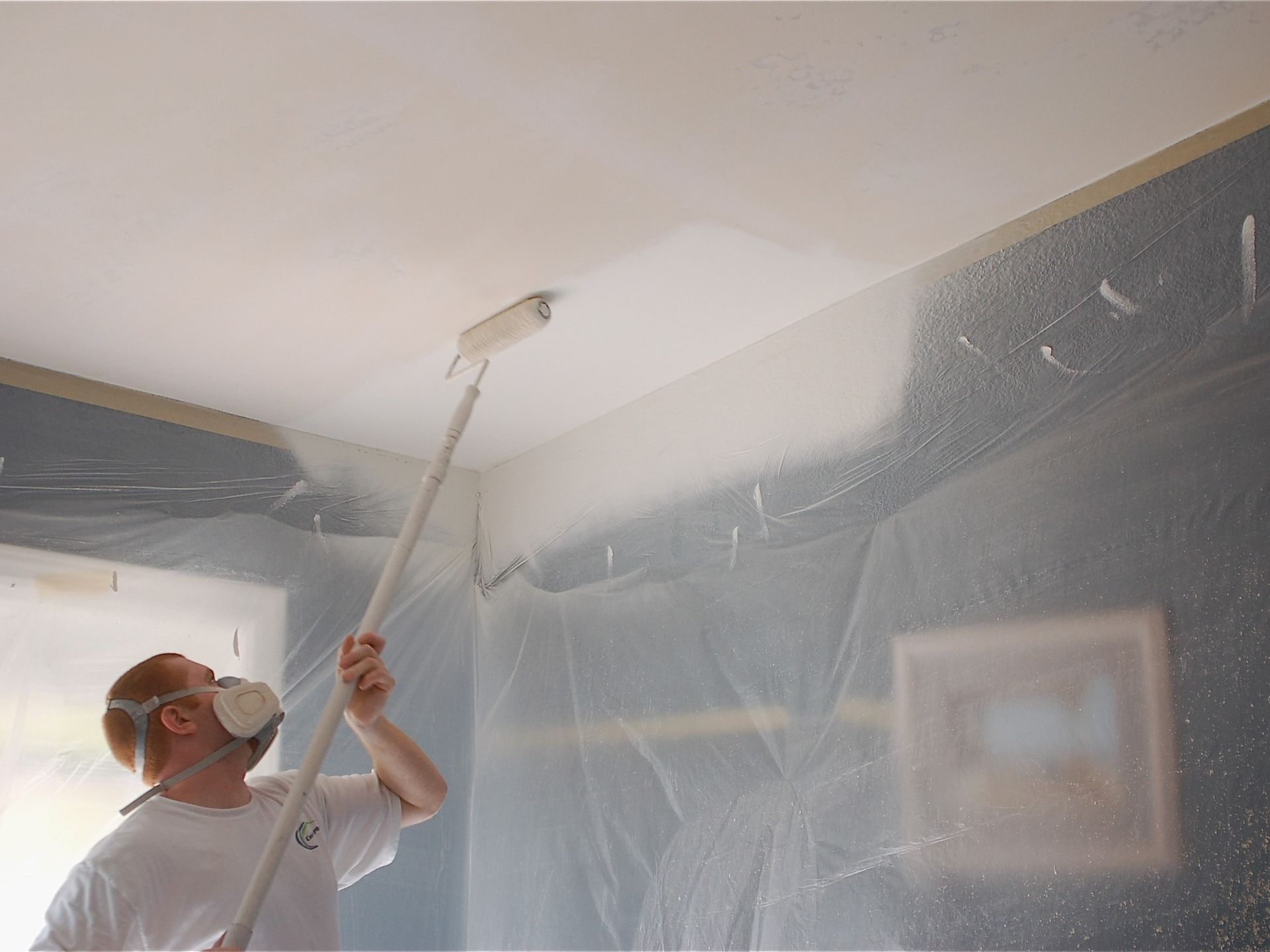 A man wearing a mask is painting the ceiling with a roller
