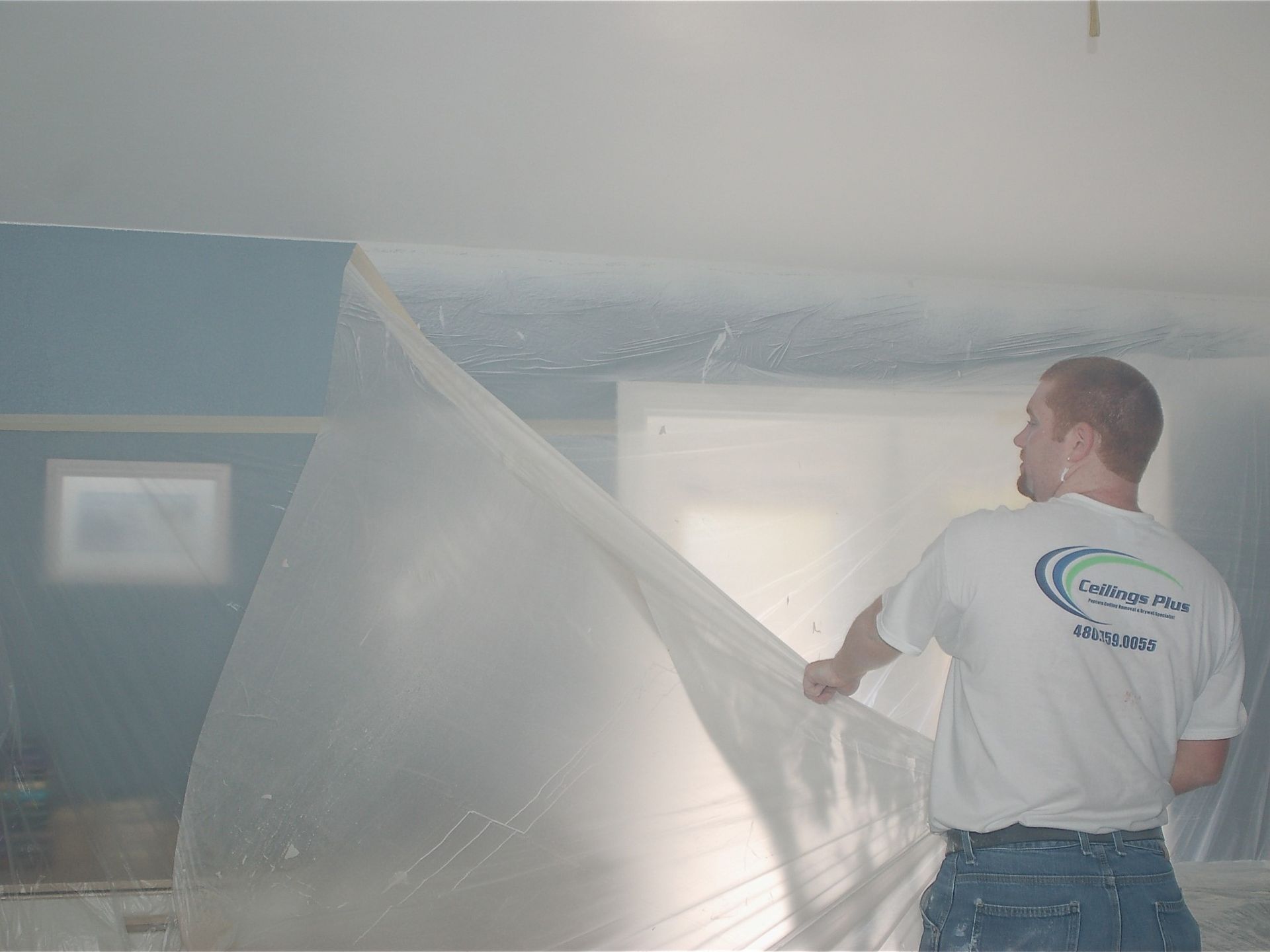 A man is covering the ceiling with a plastic sheet.