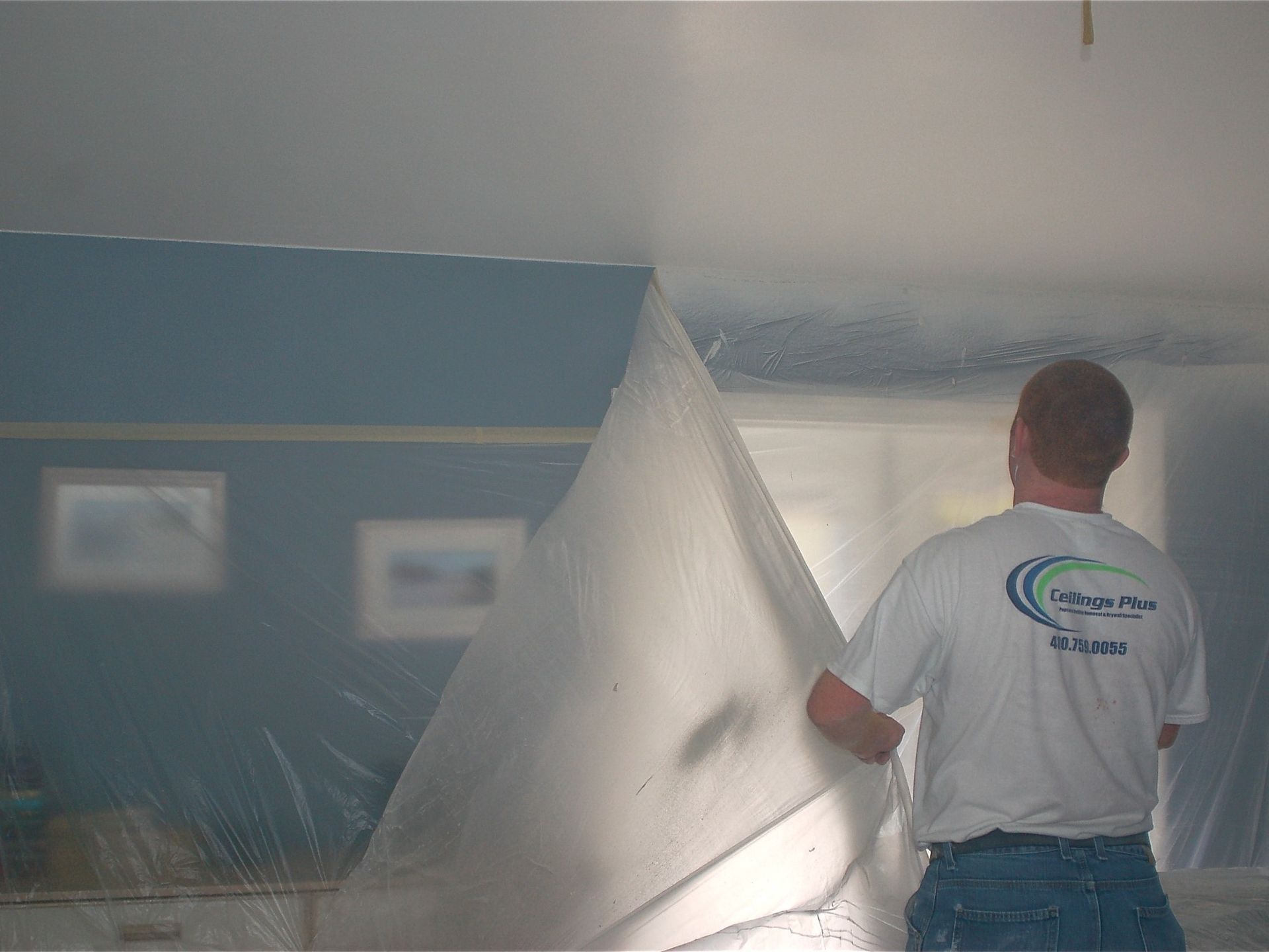 A man is covering the ceiling of a room with plastic.