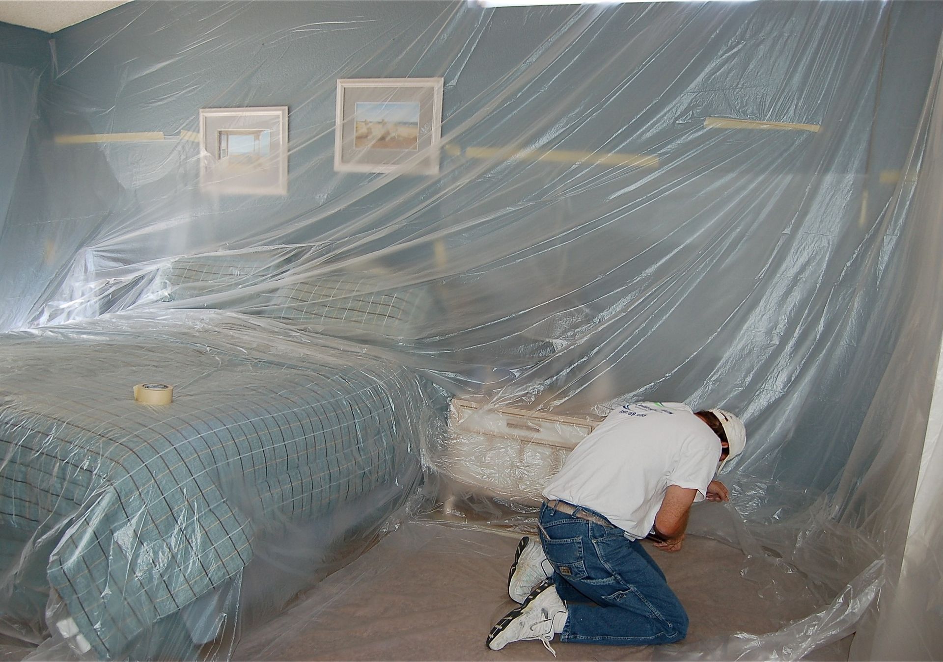 A man is kneeling under a plastic sheet in a bedroom