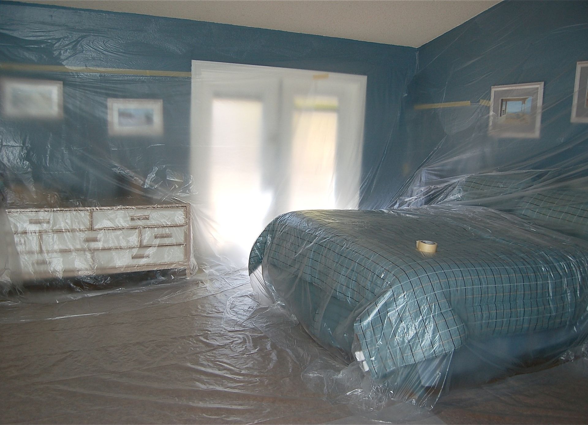 A bedroom with a bed and dresser covered in plastic