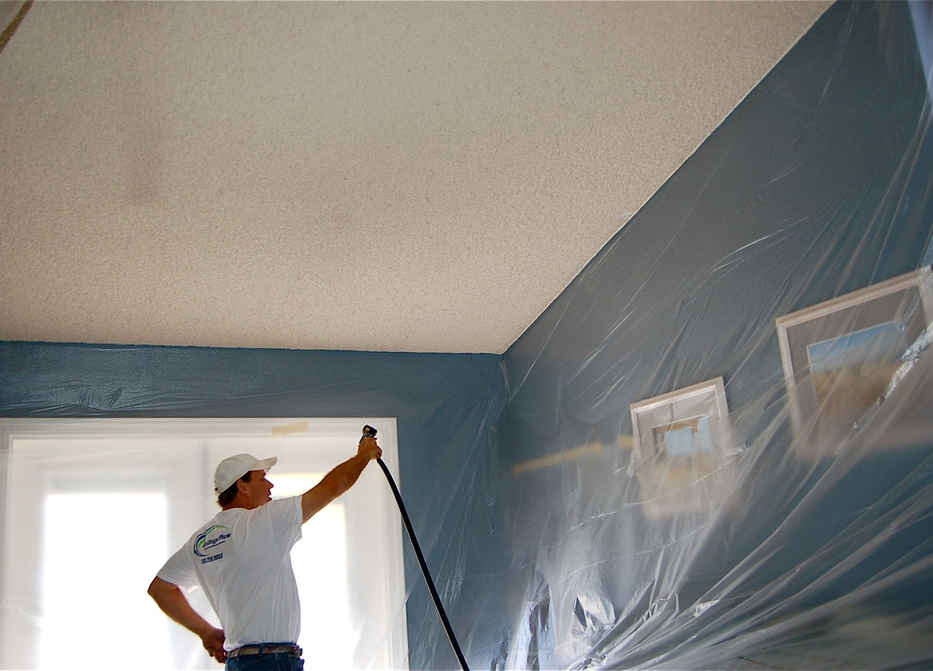 A man is painting the ceiling of a room