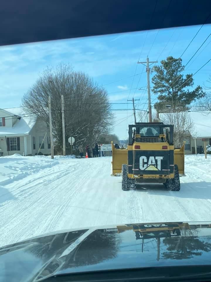 A cat snow plow is driving down a snow covered road.