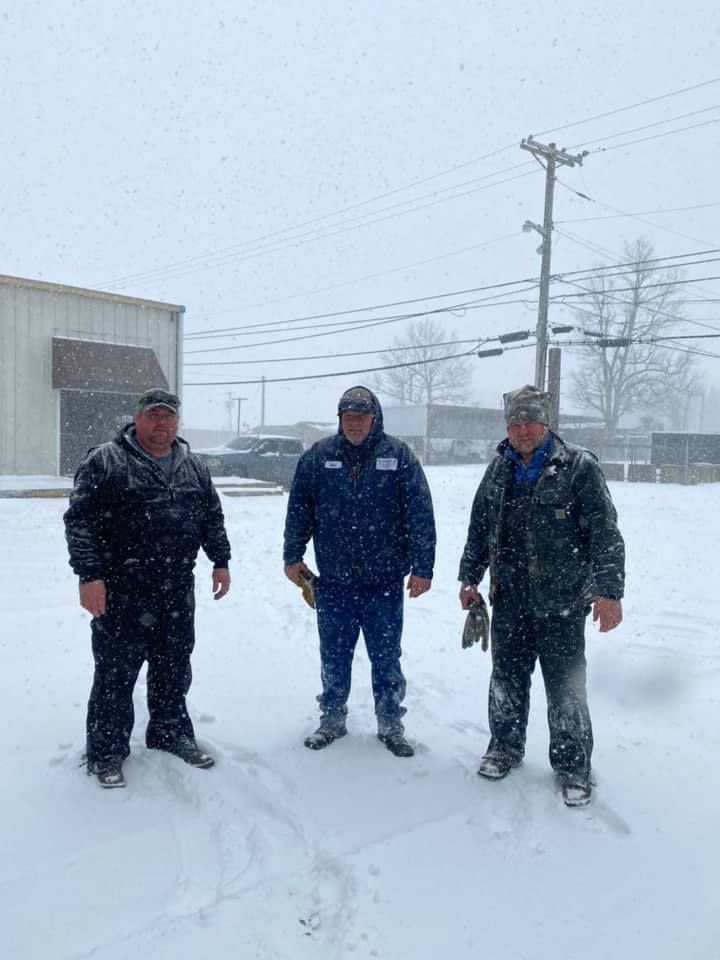 Three men are standing in the snow in front of a building.