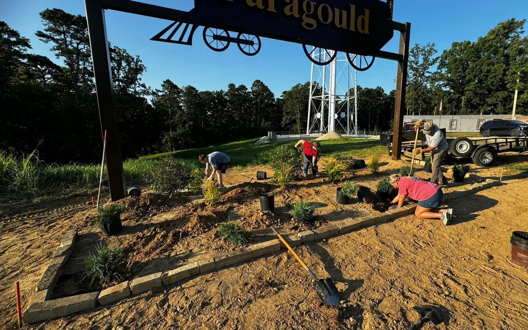 A group of people are working in a garden under a sign that says