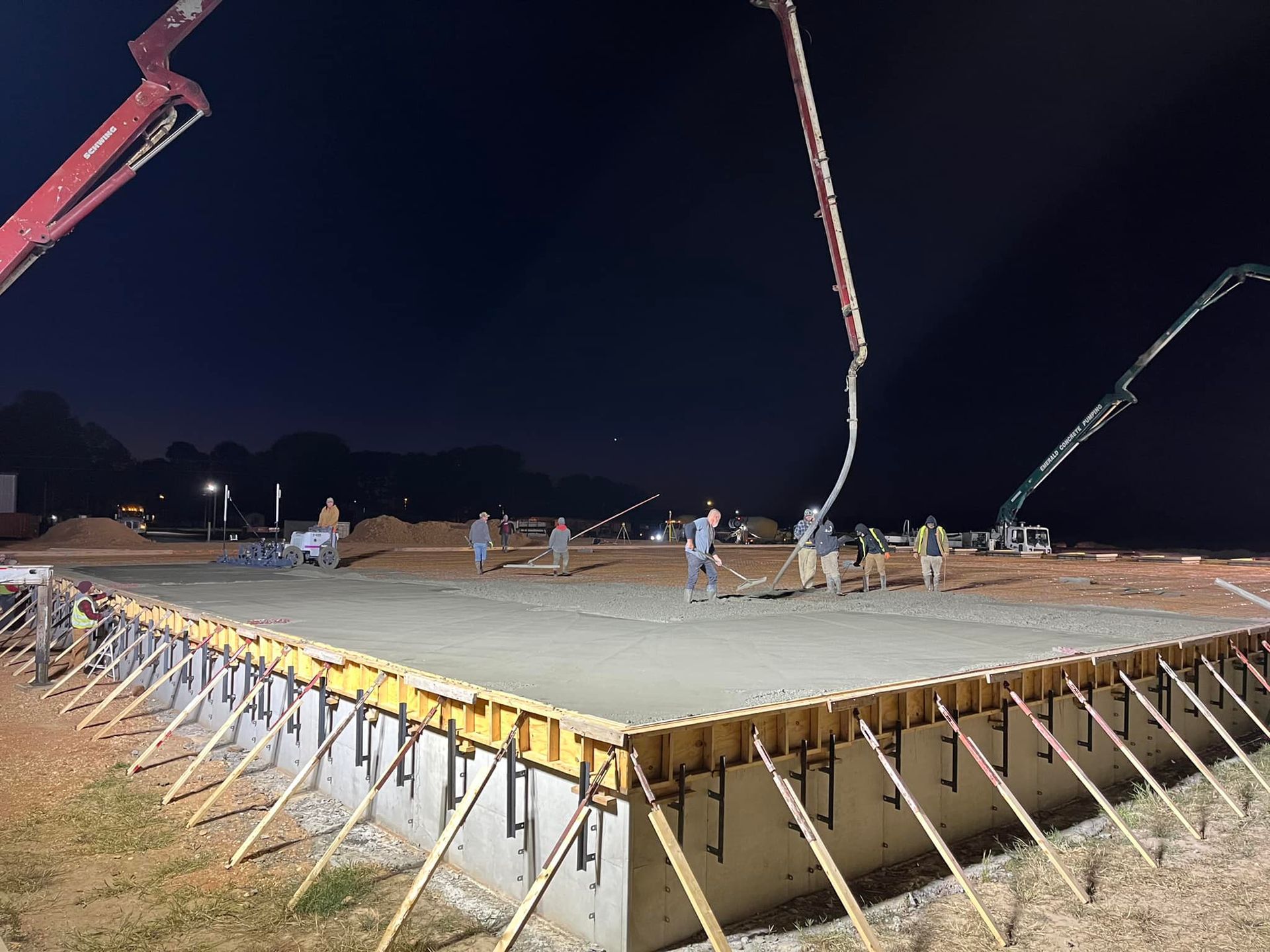 A concrete pump is pouring concrete into a foundation at night.