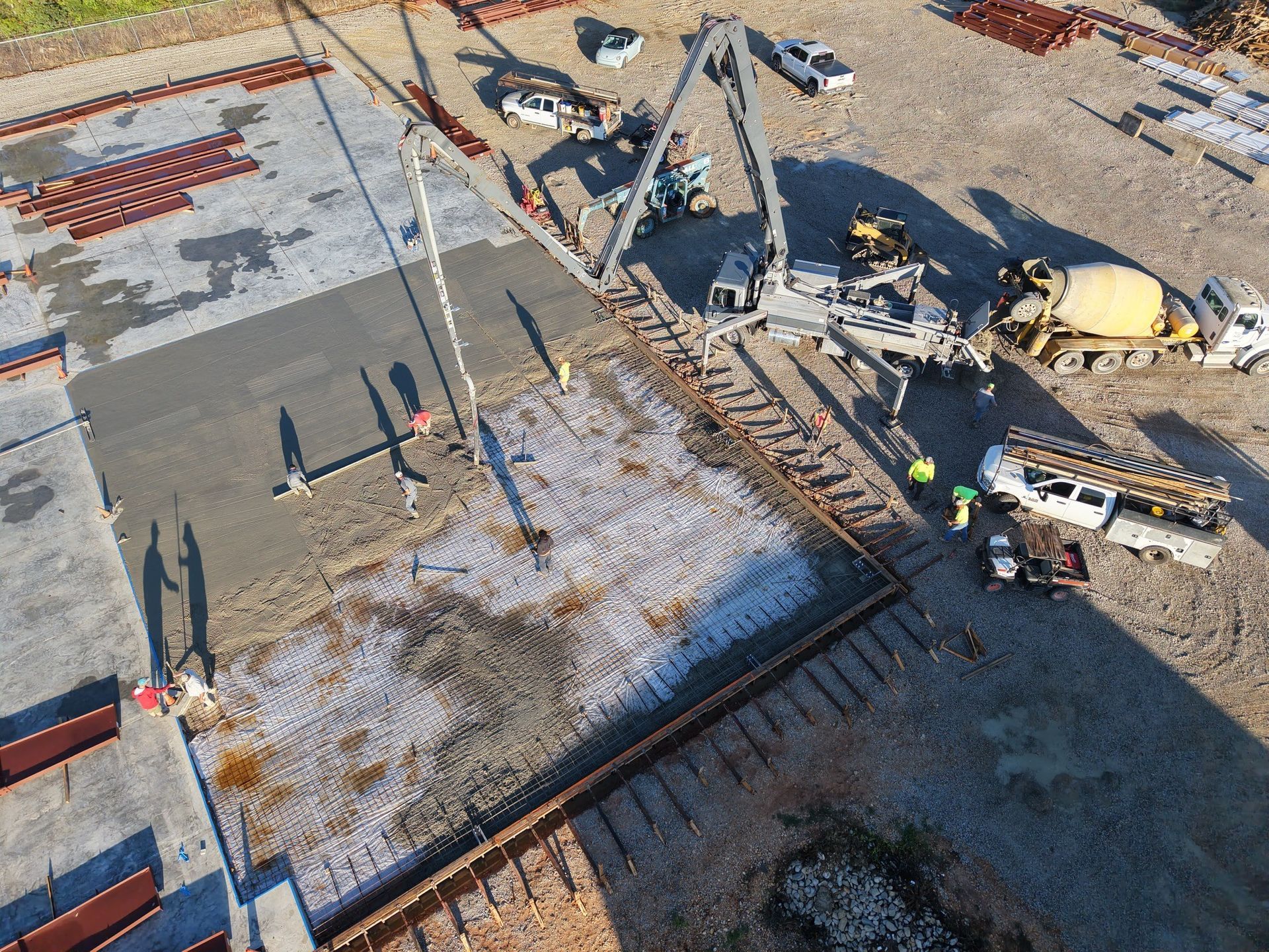 Construction site with concrete being poured by a pump truck; workers nearby.