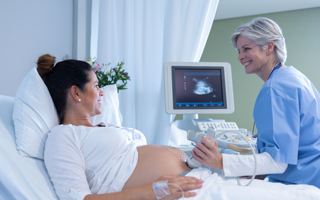 A pregnant woman is laying in a hospital bed getting an ultrasound from a nurse.