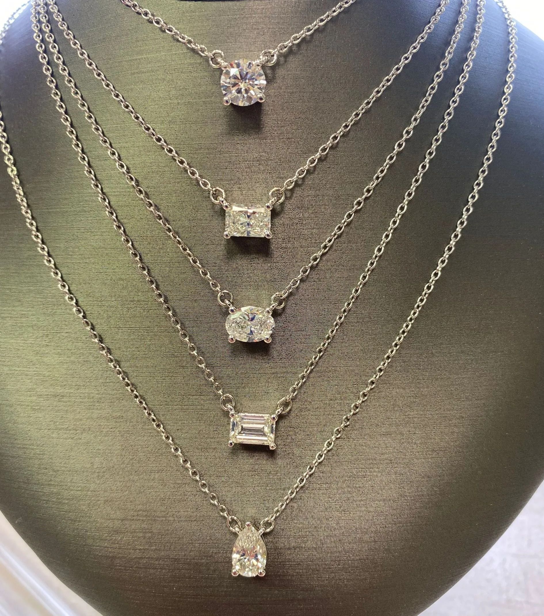 Five diamond pendant necklaces layered on a textured mannequin bust