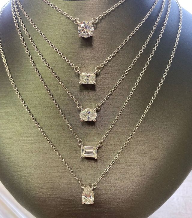 Layered silver necklaces with square and flower pendants on a dark textured display bust
