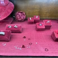 Pink jewelry display with several rings on velvet cushions and scattered heart-shaped confetti