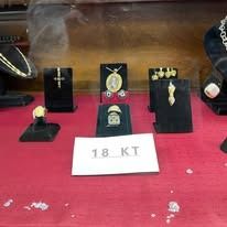 Display of gold jewelry pieces on black stands with an “18 KT” sign on a red cloth background