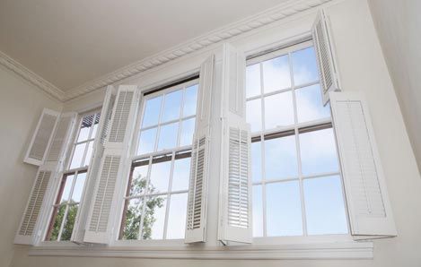 A couple of windows with shutters open in a room.