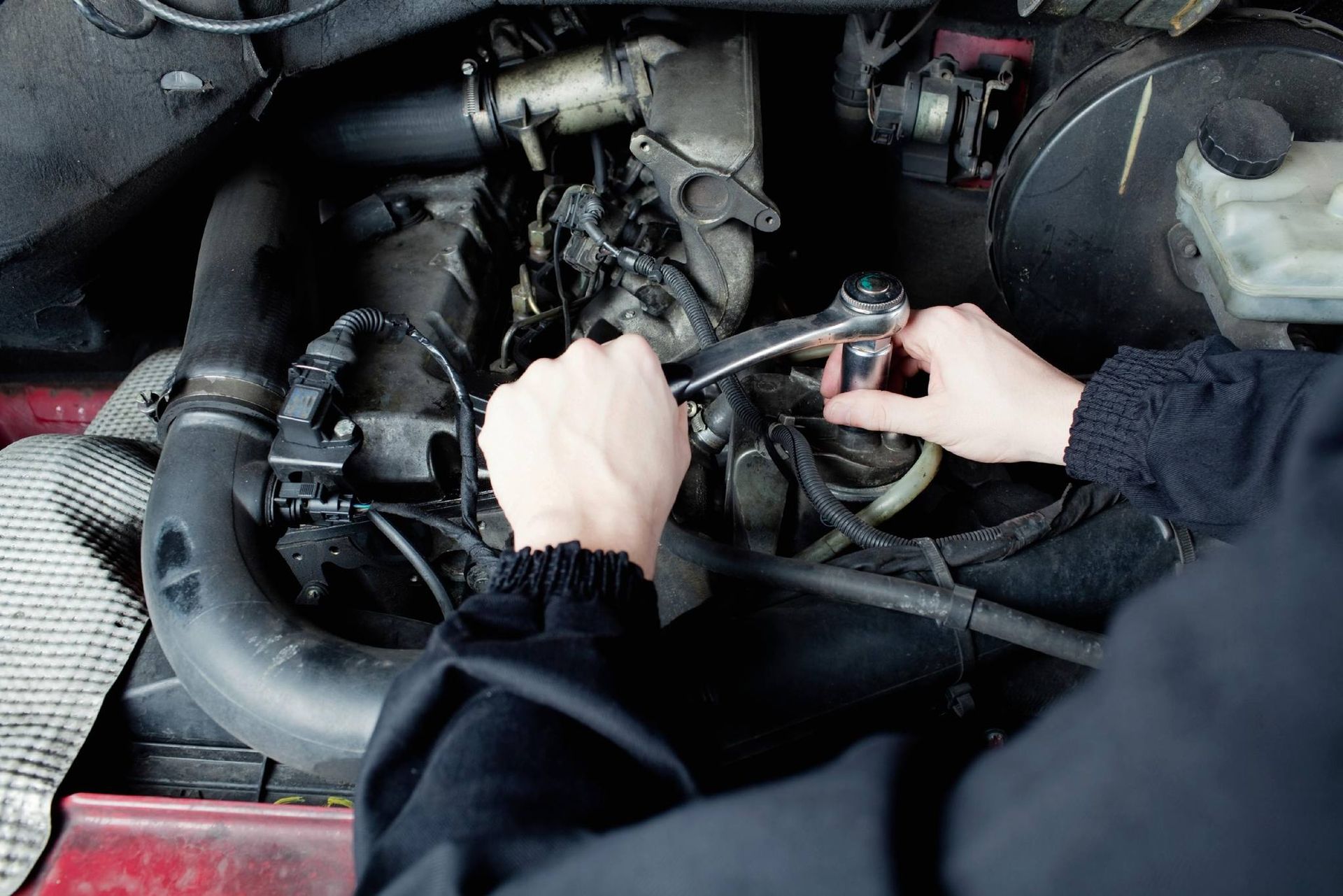 Hands using a wrench to work on a car engine.