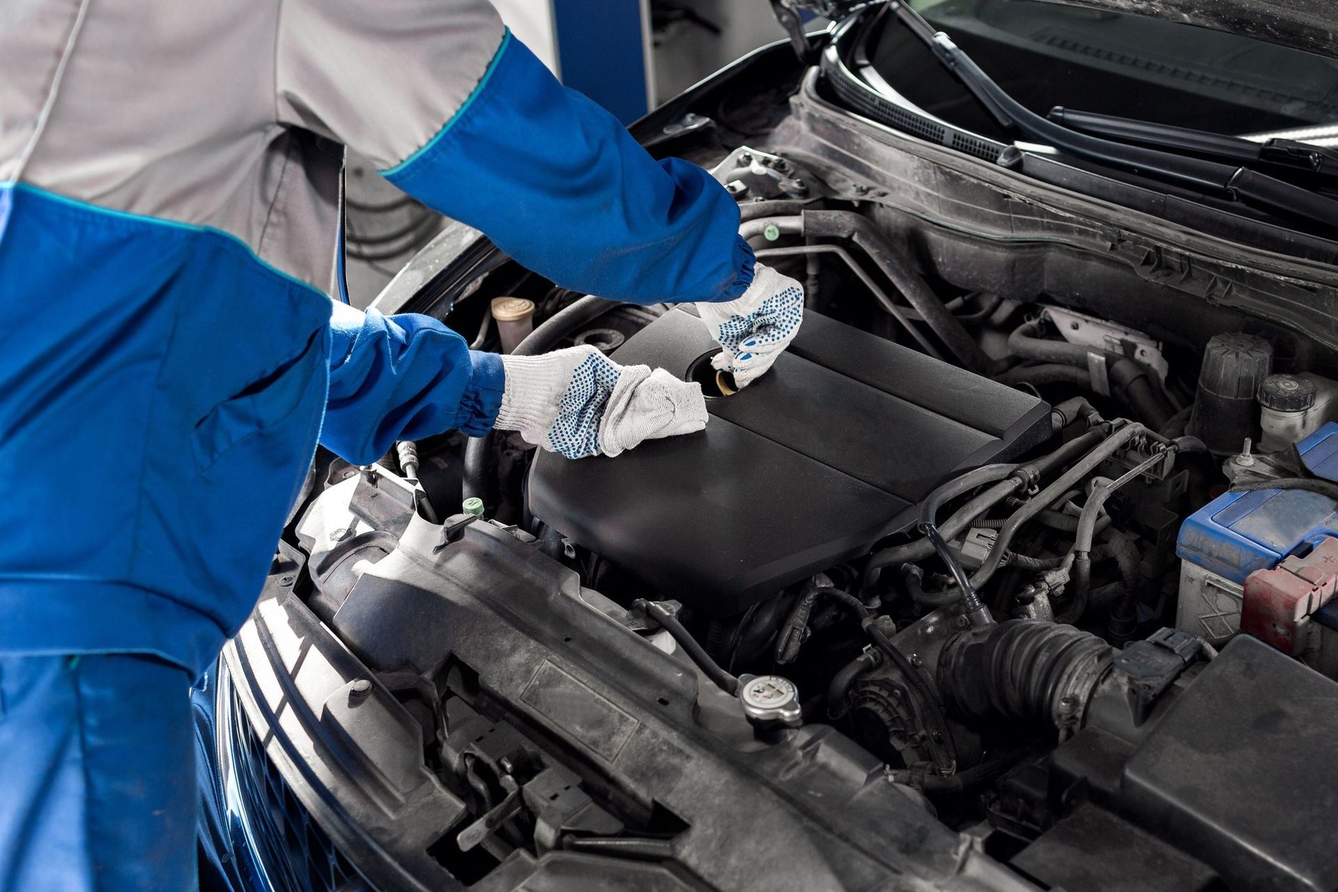 Mechanic cleaning car engine with white cloths; wearing blue gloves and uniform.