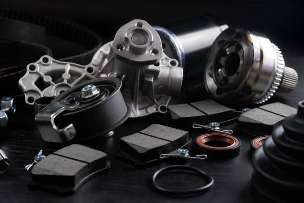 Car parts, including brake pads, water pump, and drive shaft, on a dark surface.