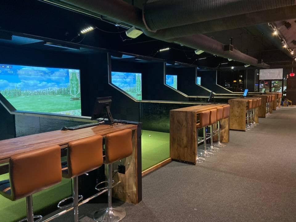 A row of bar stools and tables in a golf simulator.