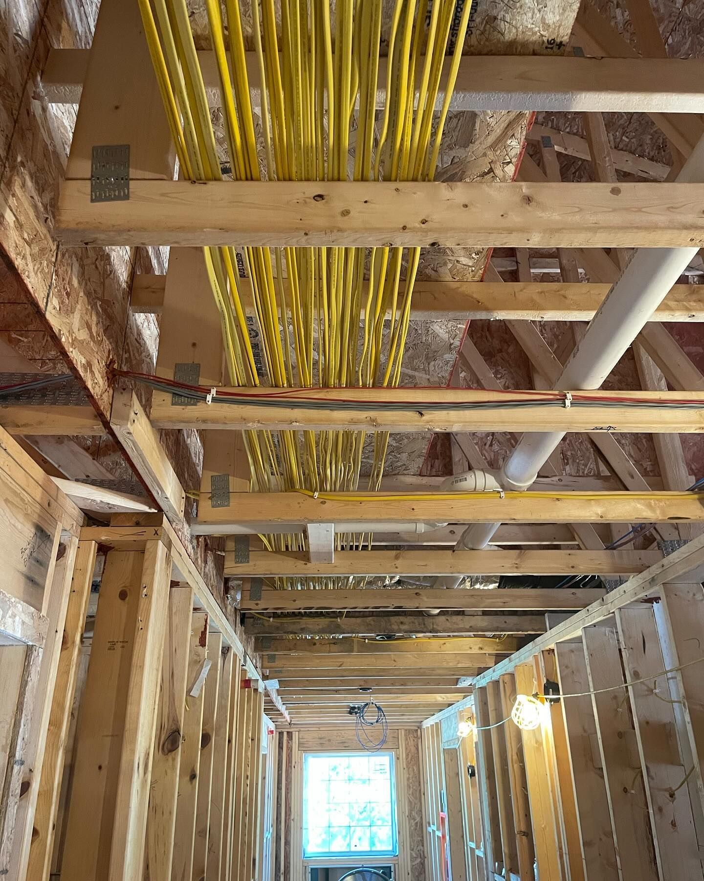 A hallway in a house under construction with yellow wires hanging from the ceiling.