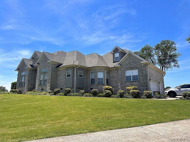 Two-story brick house with gray roof and green lawn against a blue sky.