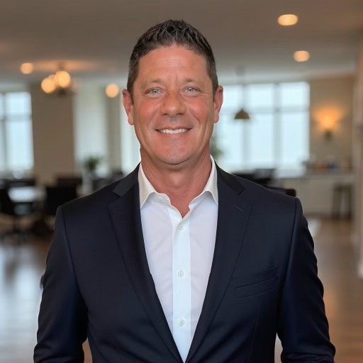 Man in suit smiles, indoors with blurred background of a modern office space.
