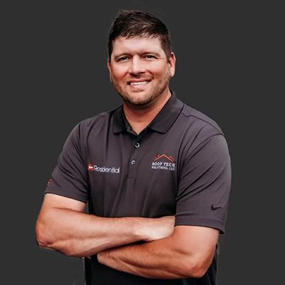 Man with arms crossed, wearing a gray polo shirt, smiling, with logo 