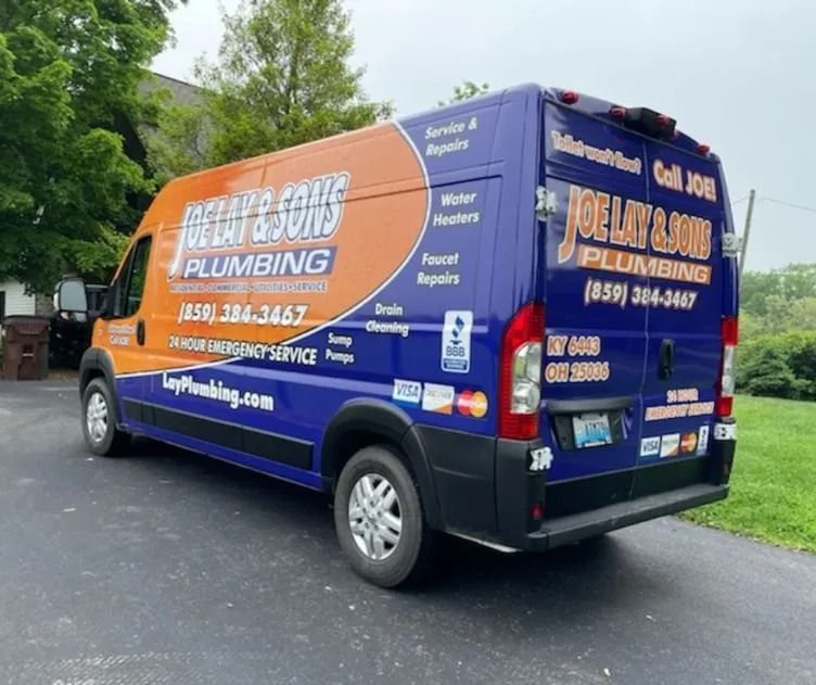 A Joe Lay & Sons Plumbing service van, orange and blue, parked on a driveway with listed services and phone number.