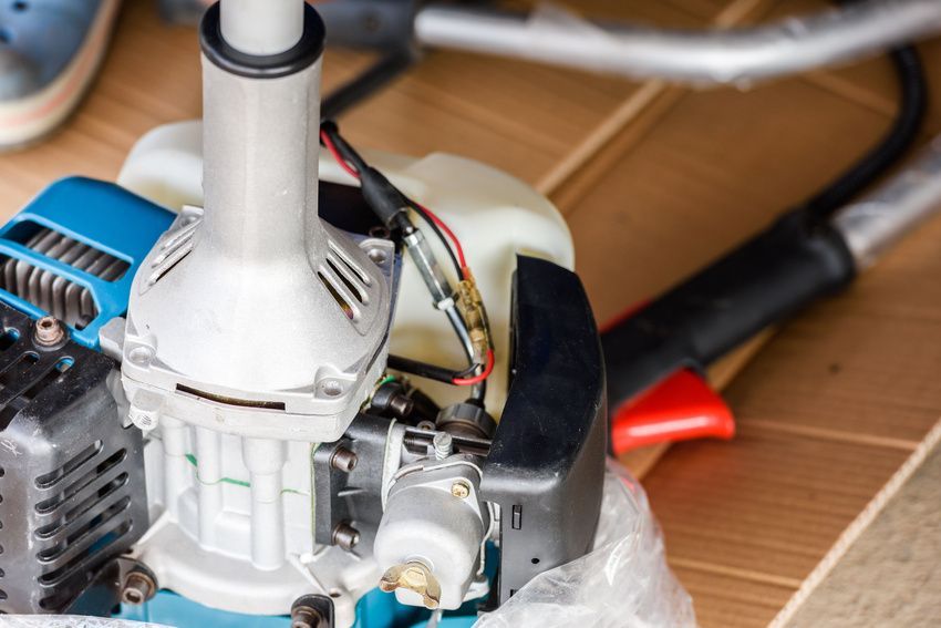 A close up of a lawn mower engine on a wooden floor.