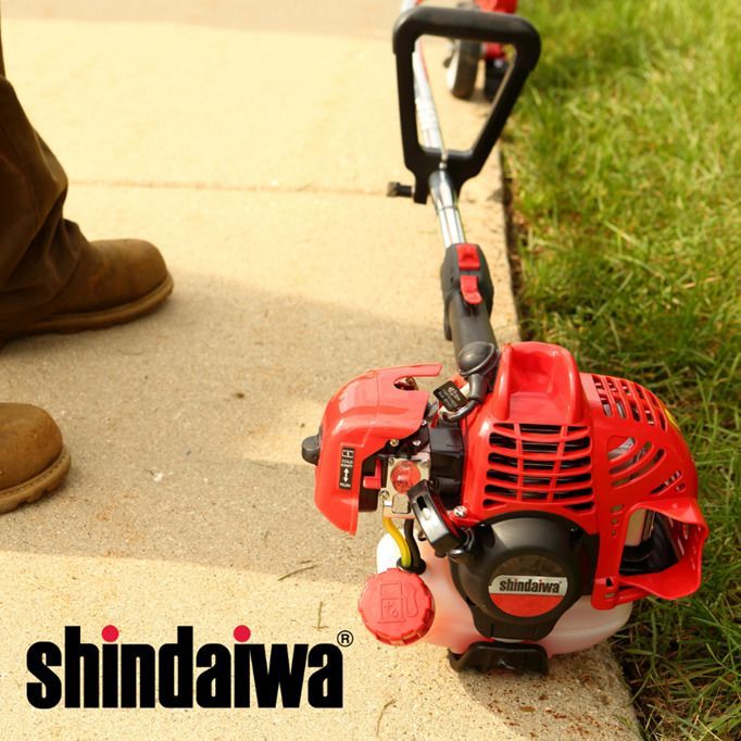 A red shindaiwa lawn mower is sitting on the sidewalk