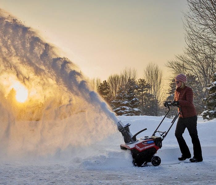 A woman is blowing snow with a snow blower.