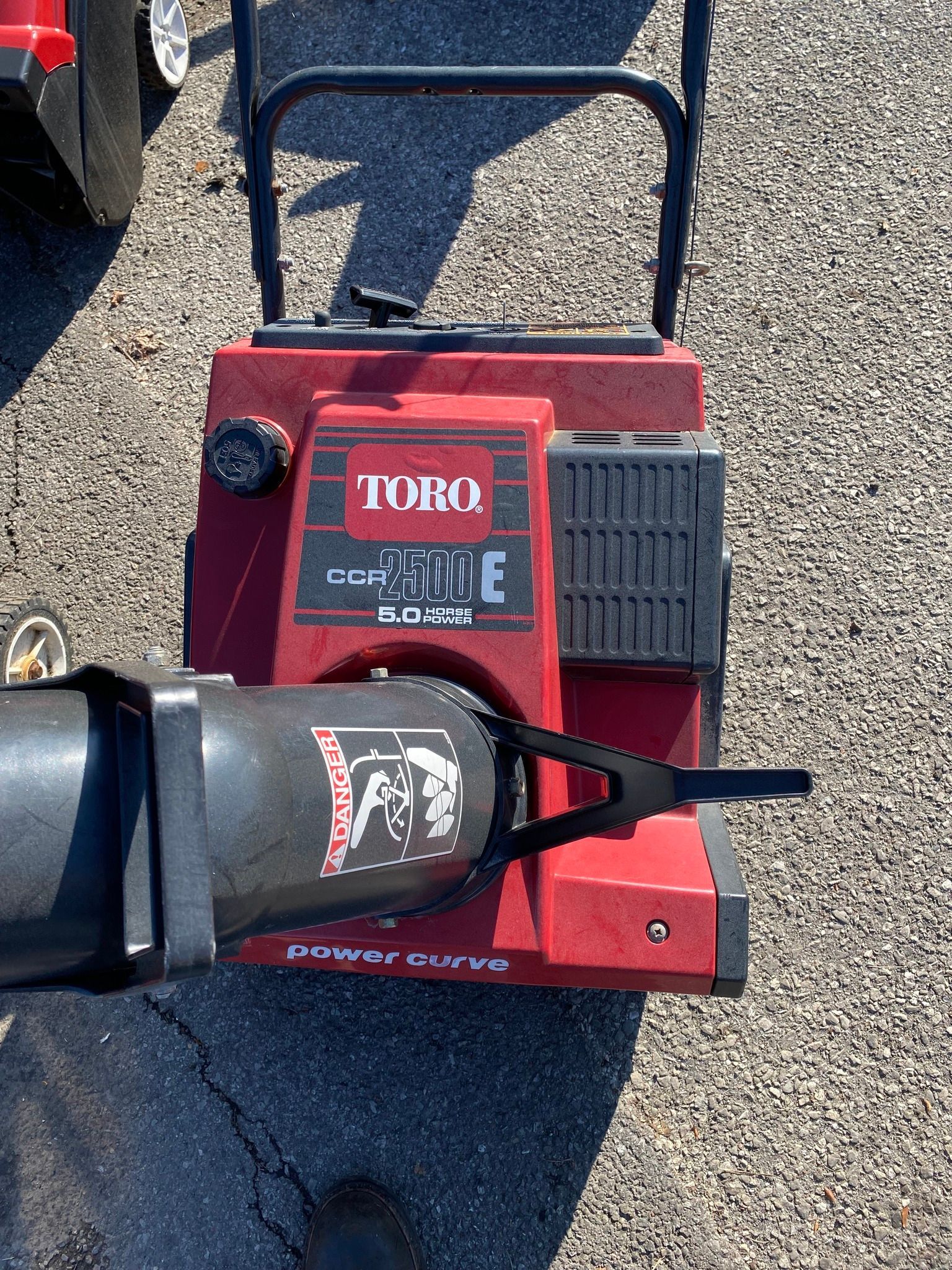 A red and black snow blower is sitting on the ground.