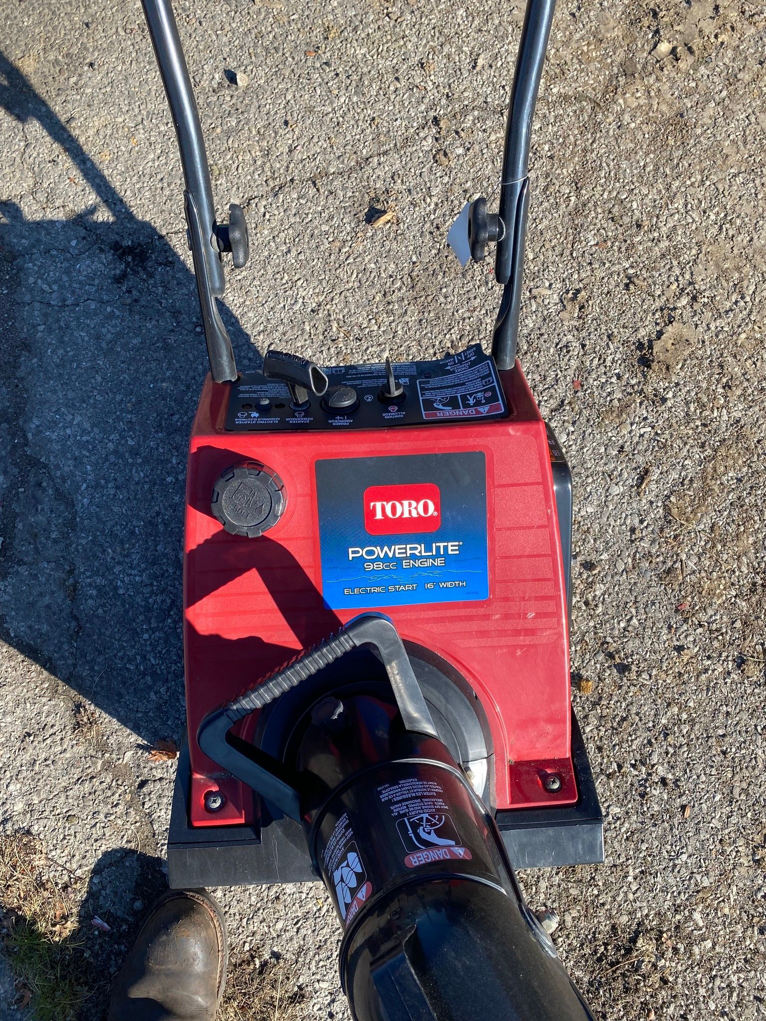 A red and black snow blower is sitting on the ground.