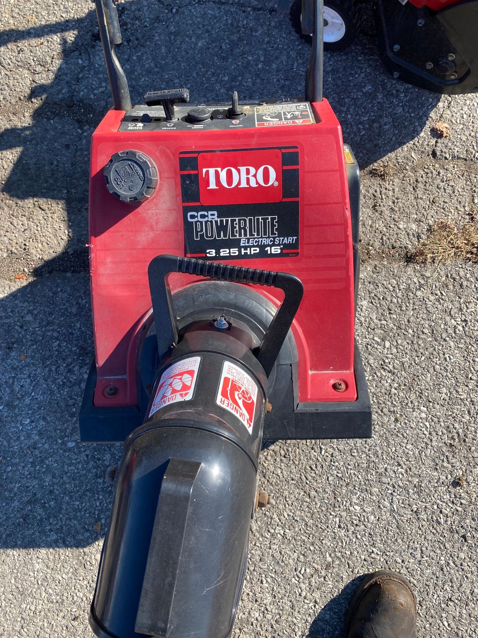 A red and black snow blower is sitting on the ground.