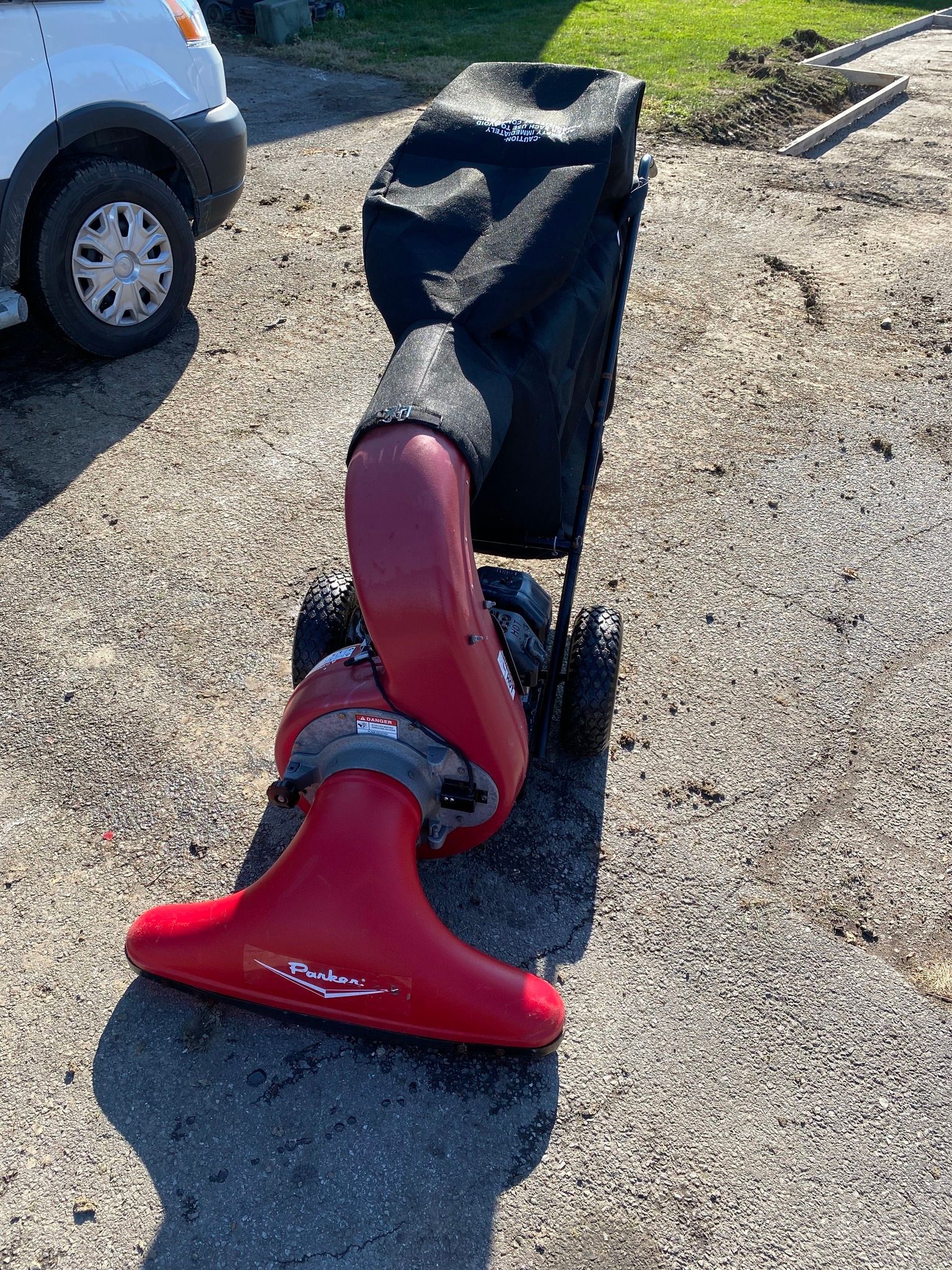 A red vacuum cleaner is sitting on the ground next to a white van.