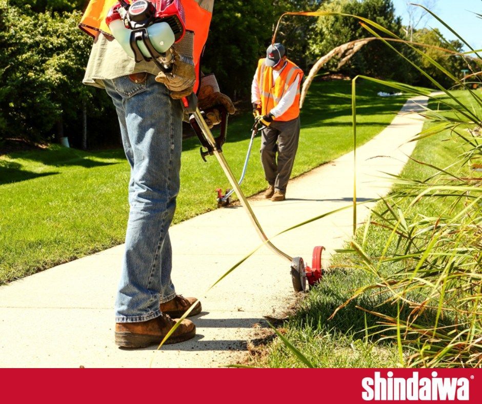 A man is using a lawn mower on a sidewalk next to a sign that says shindaiwa