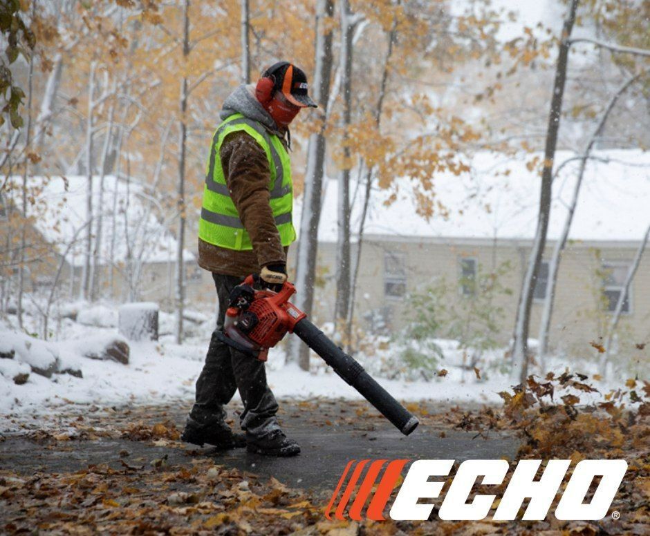 A man is blowing leaves on a snowy road with echo in the background