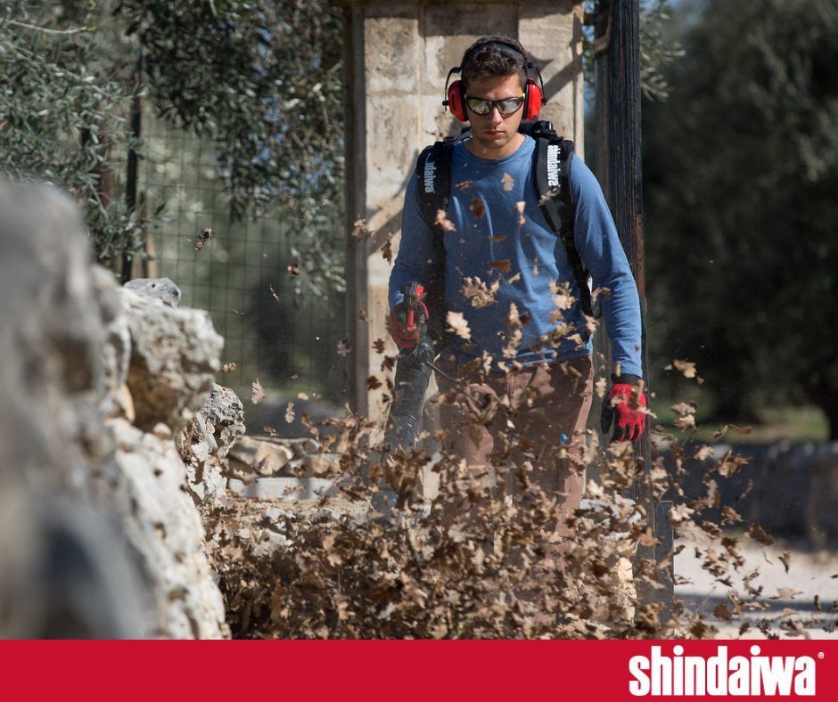 A man wearing headphones is blowing leaves with a blower.