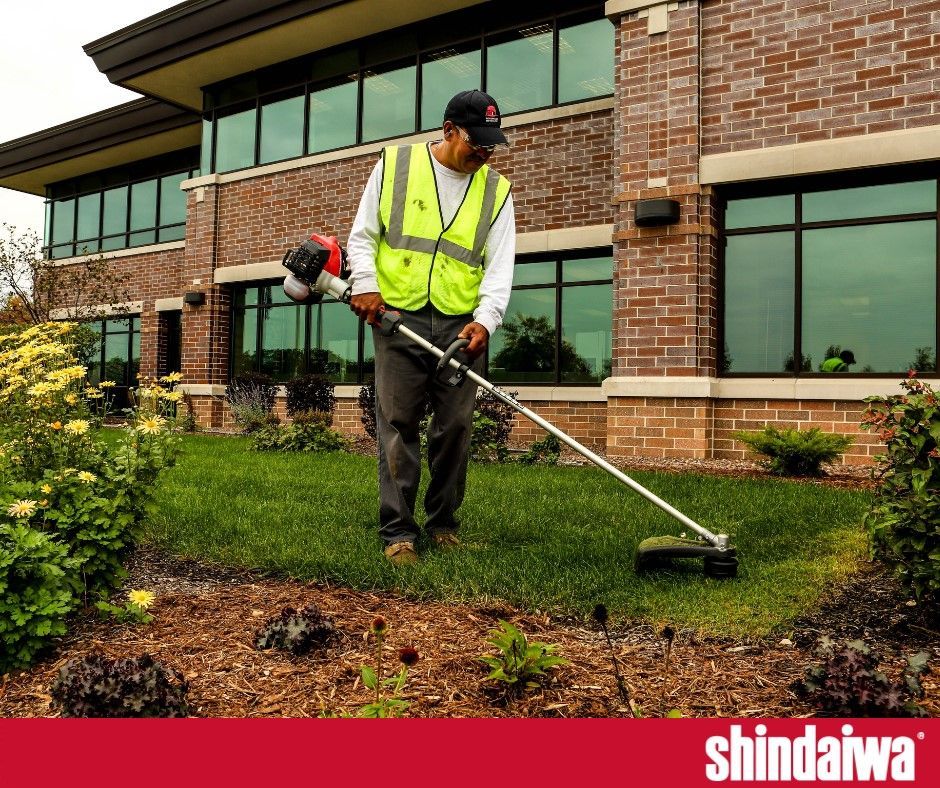 A man is using a lawn mower in front of a brick building