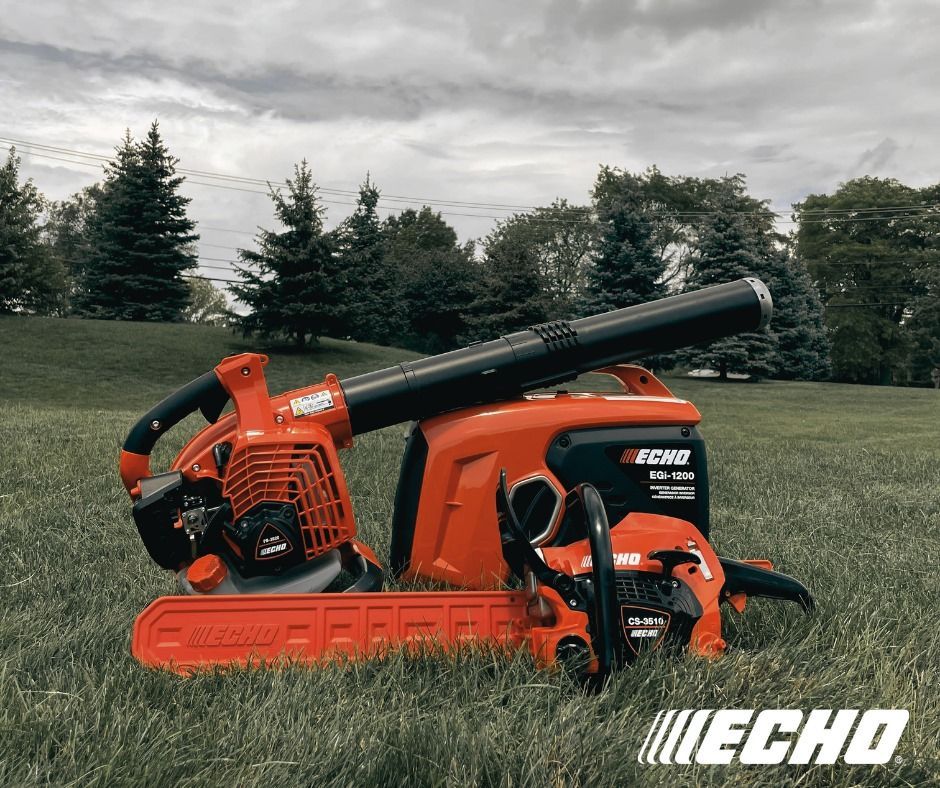 A chainsaw and a leaf blower are sitting in a grassy field.