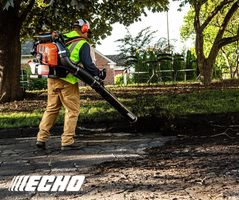A man is using a backpack blower on a sidewalk.