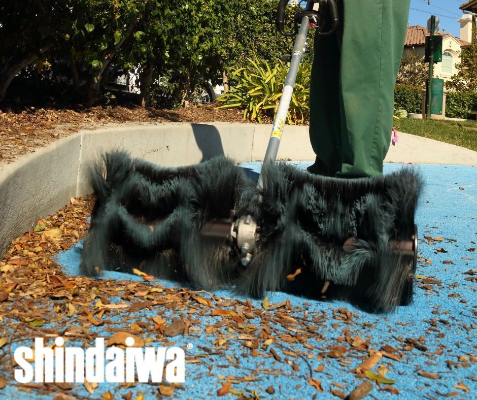 A person is sweeping leaves with a brush from shindaiwa