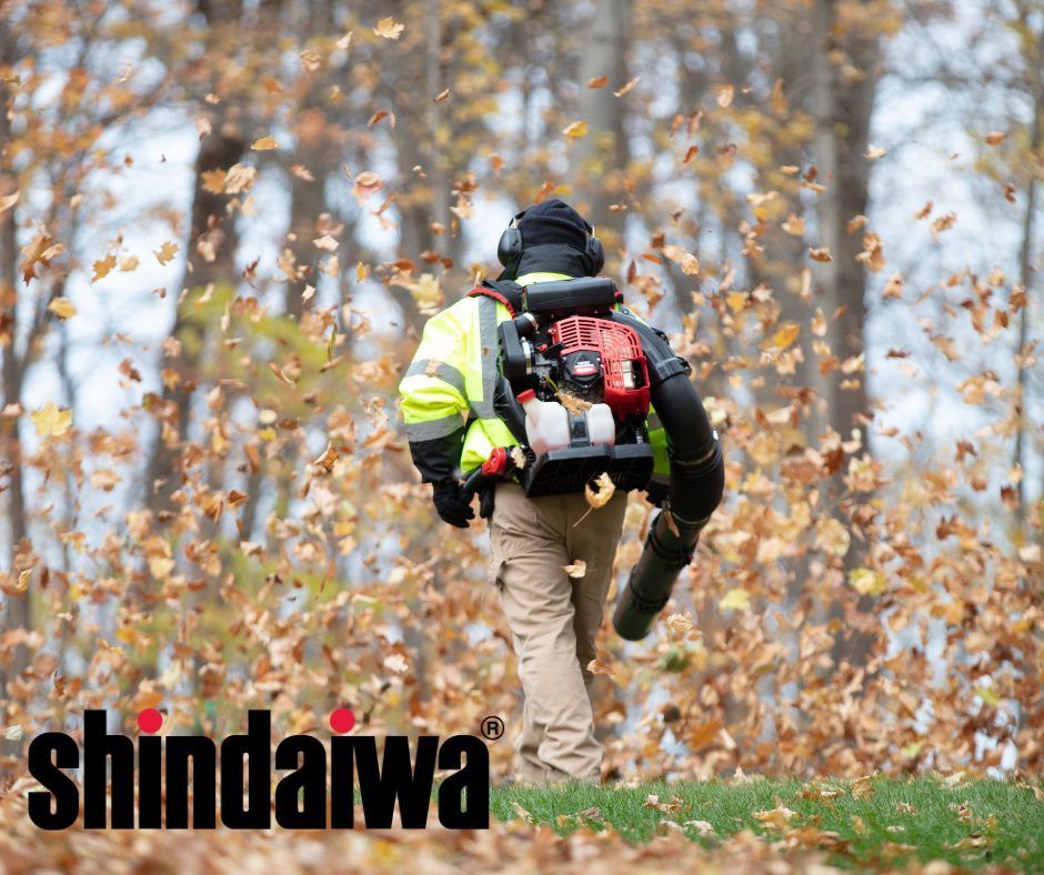 A man is blowing leaves in a forest with a shindaiwa logo in the background.
