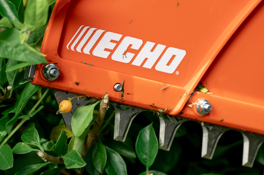 A close up of an echo hedge trimmer cutting a bush.