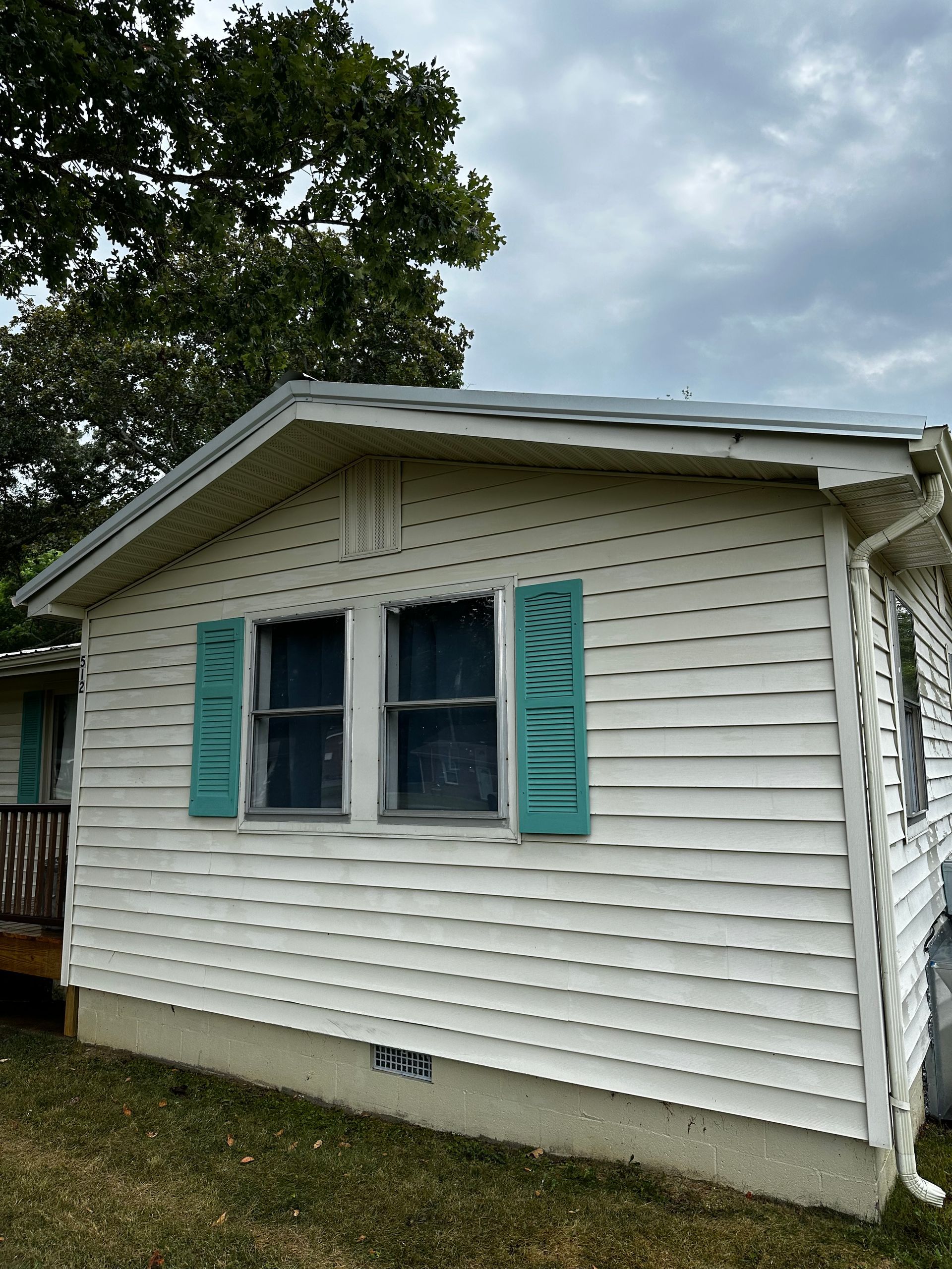 White cottage with teal shutters under a cloudy sky.