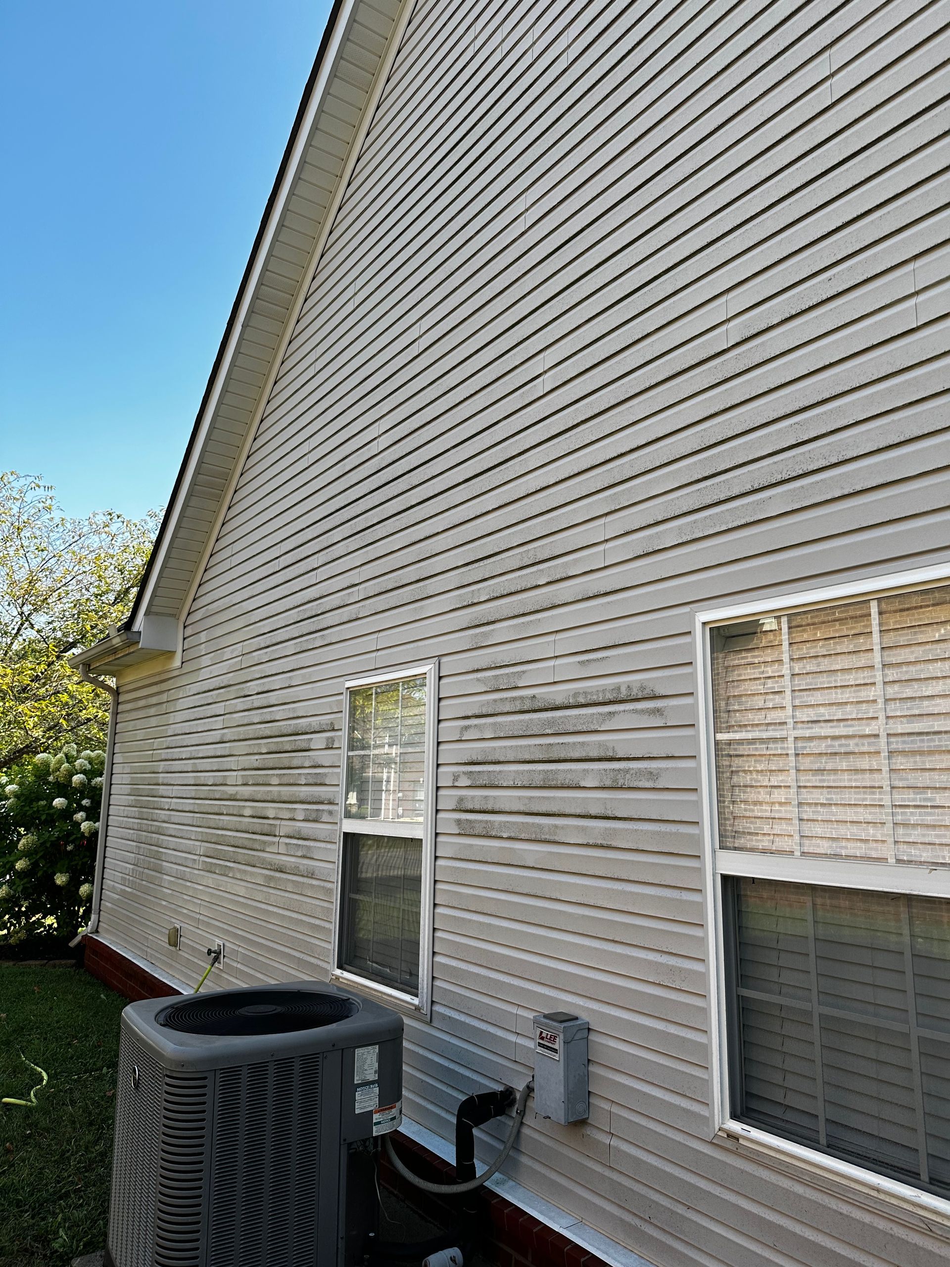 A house with light-colored siding, two windows, and an air conditioning unit.