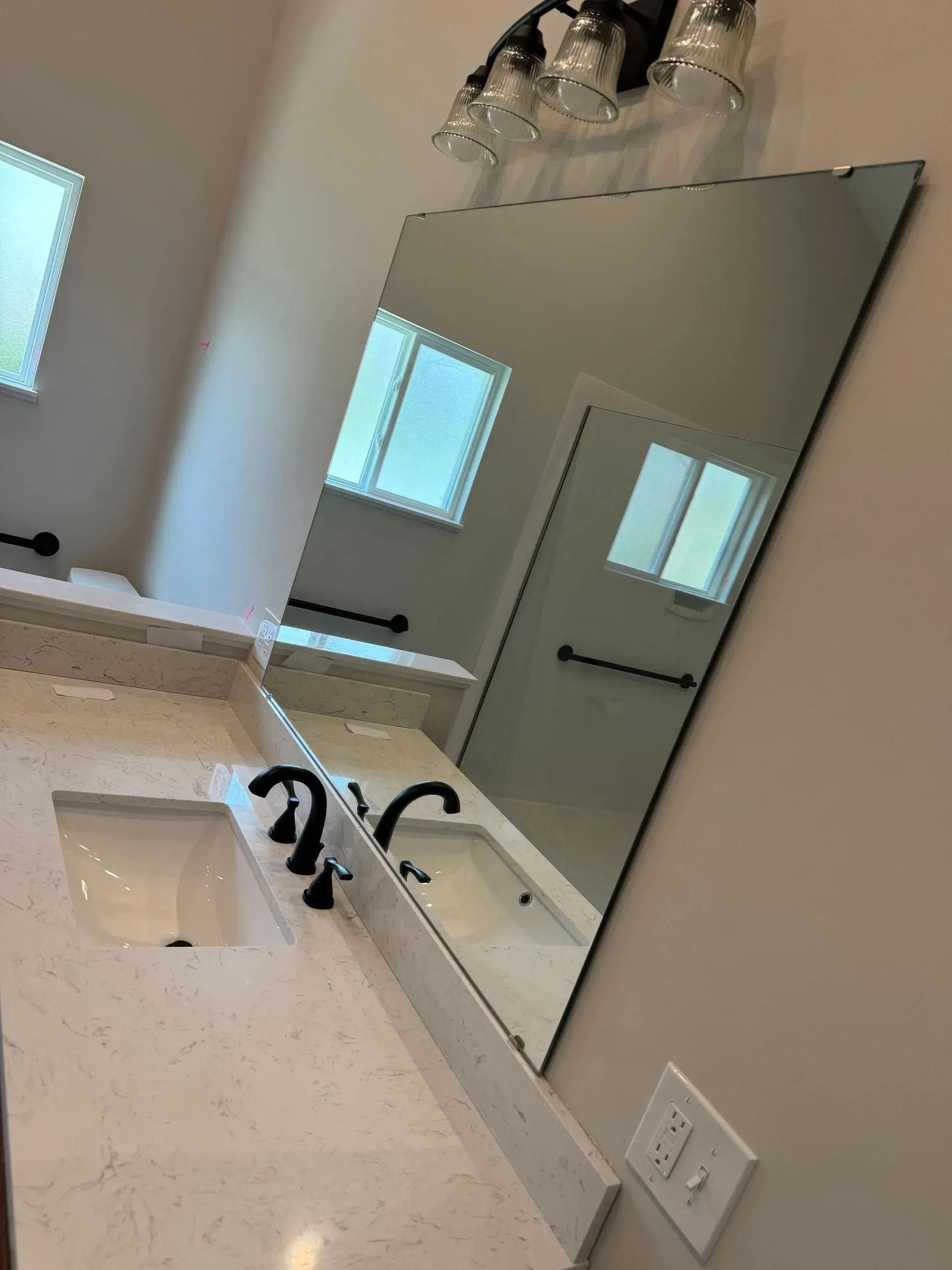 Bathroom vanity with white countertop, sink, black faucet, and large wall mirror by a window.