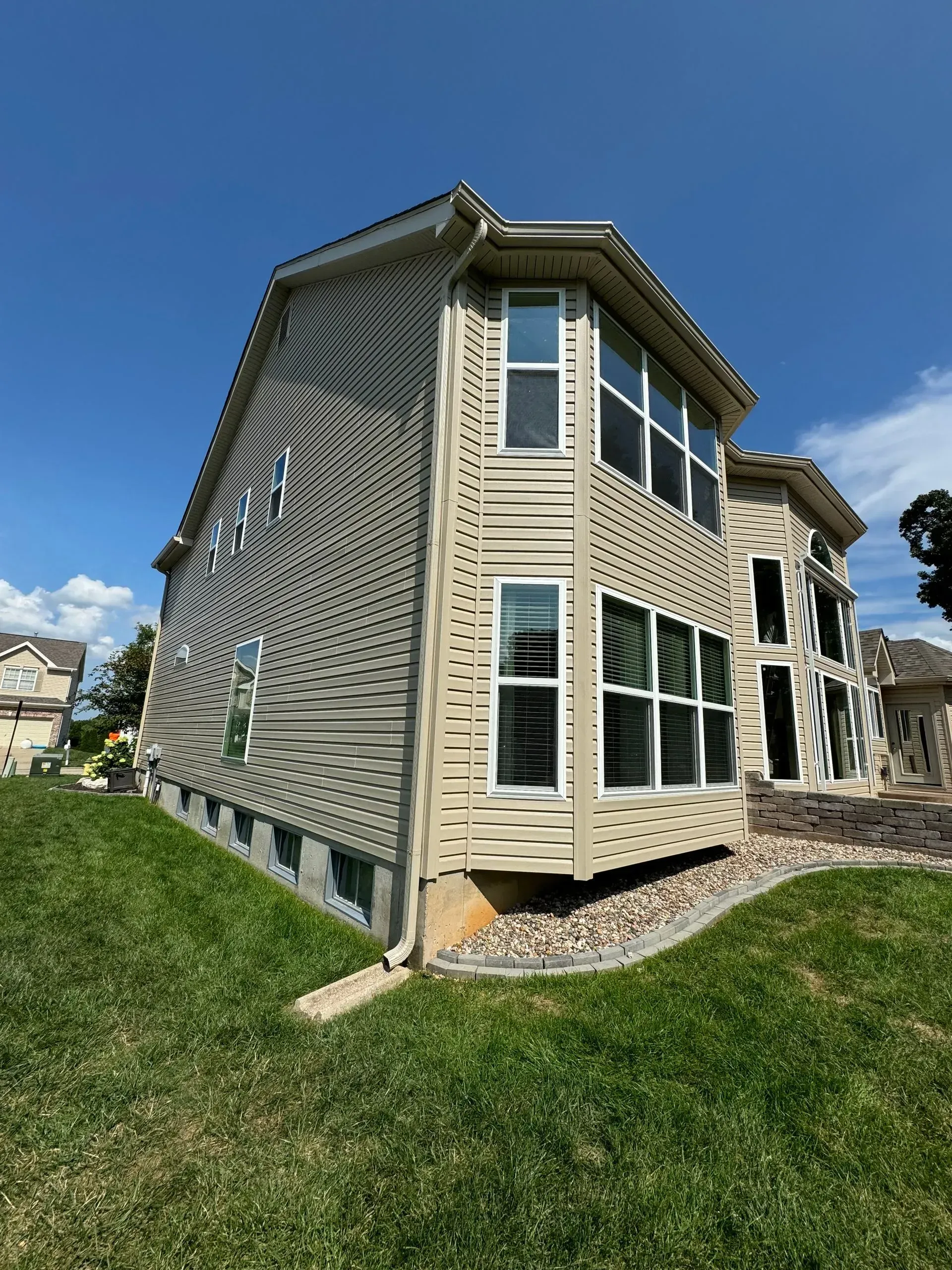 Beige house with curved facade, patterned side wall, and large windows on a grassy lot under a blue sky