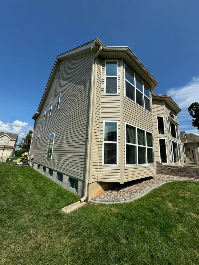 Beige house with curved facade, patterned side wall, and large windows on a grassy lot under a blue sky