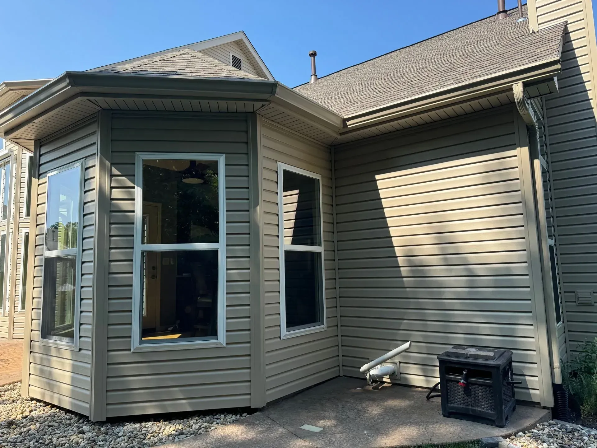 Back of a beige house with a bay window and small patio under a clear blue sky
