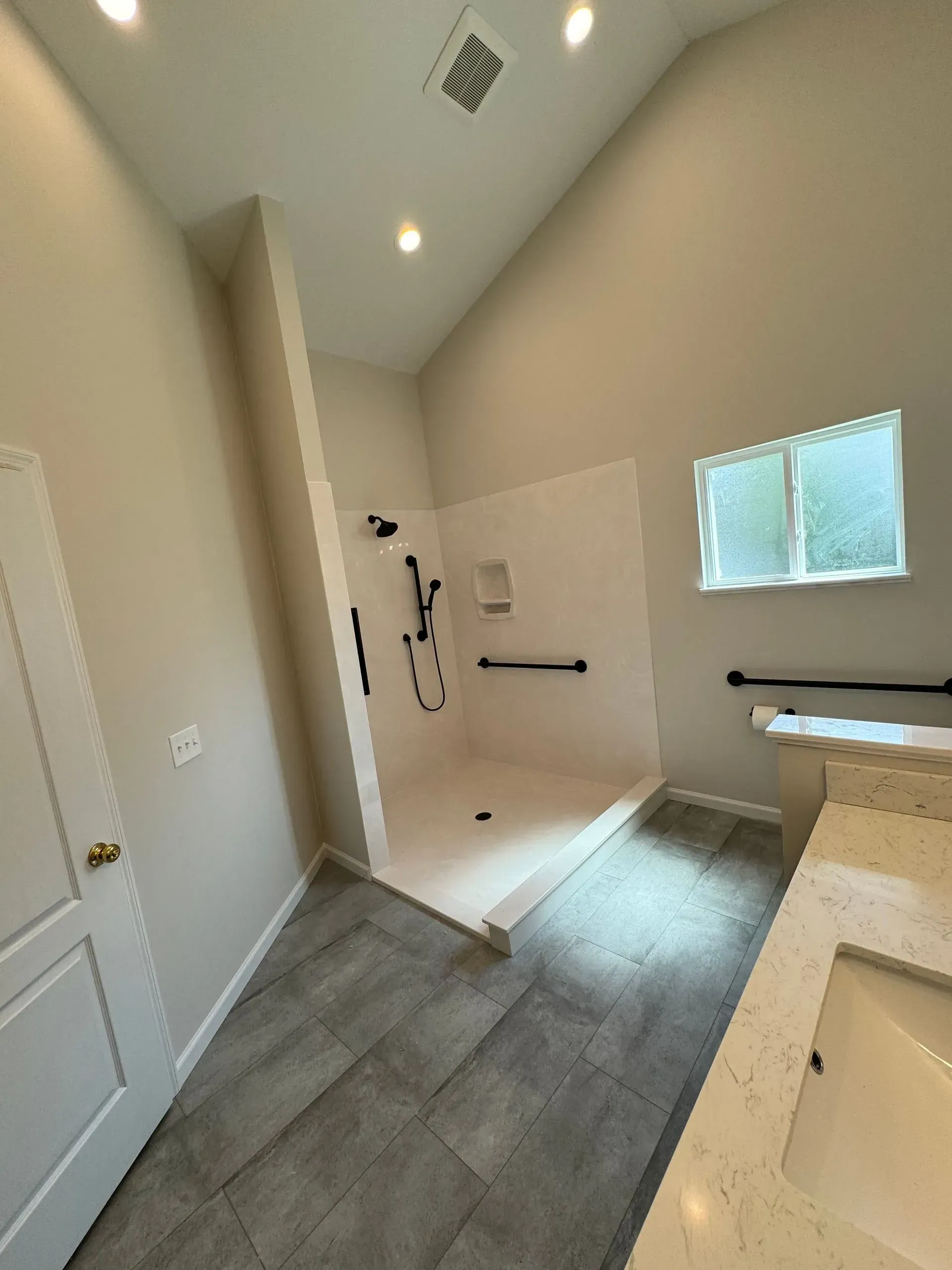 Empty bathroom with walk-in shower, gray tile floor, vanity, and small window.